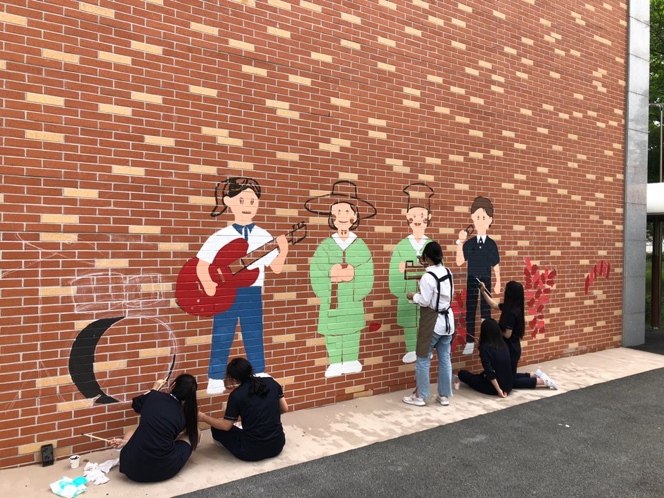 학교 건물 외벽에 벽화를 그리는 학생들의 모습
